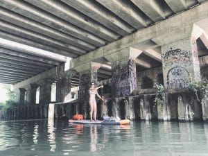 une femme passe en paddle sur une rivière sous un pont