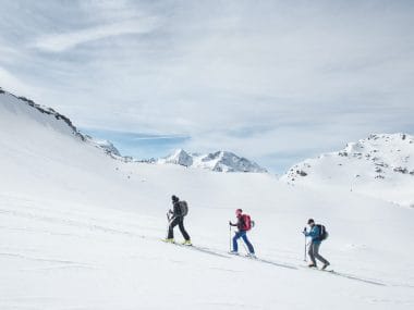 3 skieurs randonnent dans la neige sous le soleil