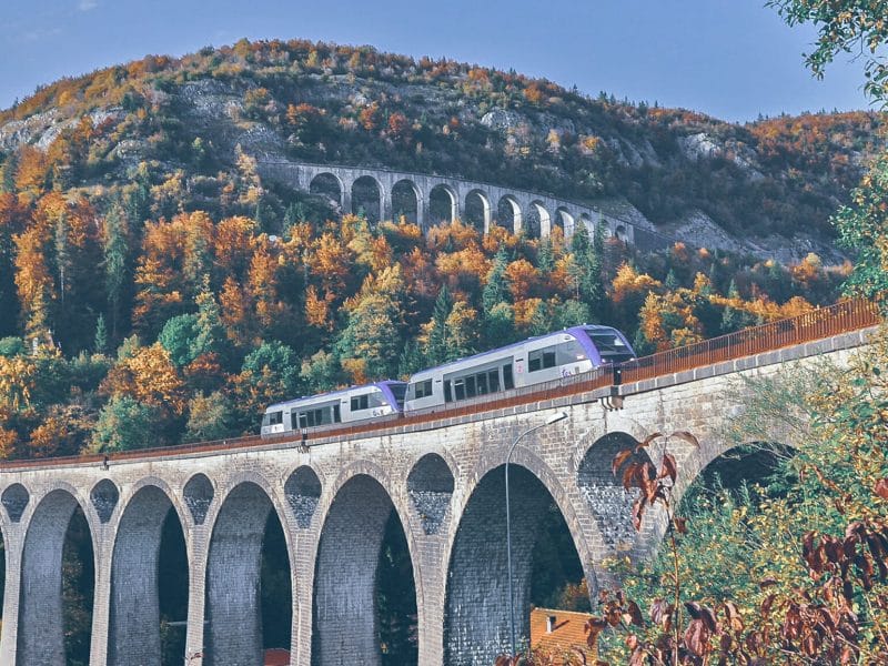 un train passe sur un viaduc dans un paysage de collines verdoyantes en automne