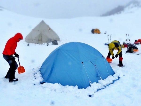 deux personnes montent leur tente dans la neige