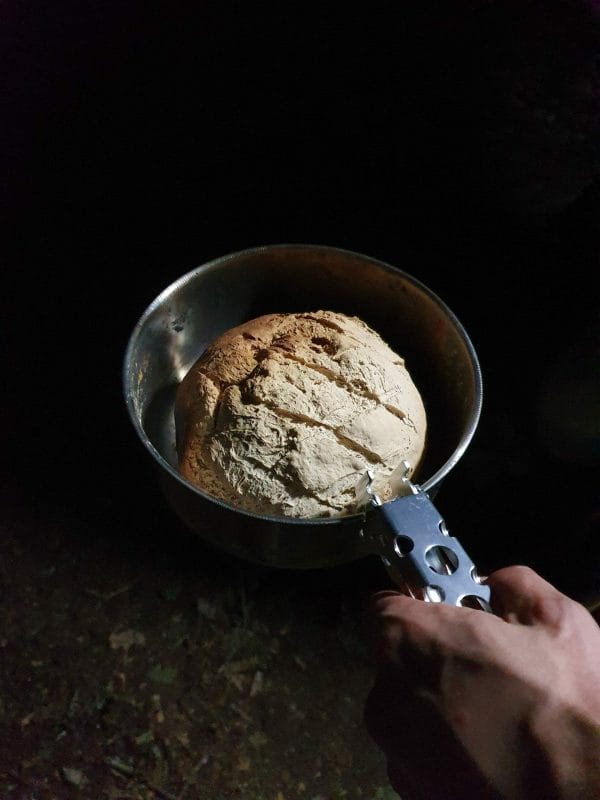 une main tient une casserole remplie d'un pain en pleine forêt
